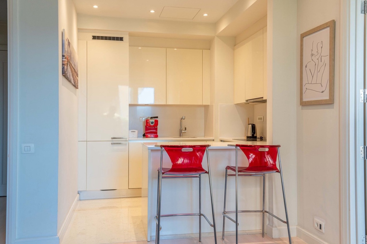 Modern kitchen in an apartment in Porto Montenegro, Tivat, Montenegro: light cabinetry and bright red bar stools.