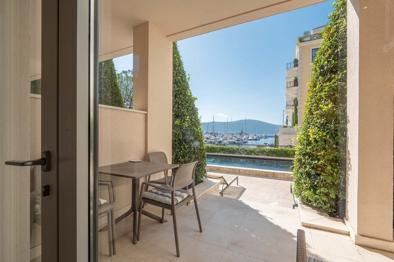 Terrace with furniture and views of the marina and yachts in Porto Montenegro, Tivat, Montenegro. Nearby pool and landscaped grounds.