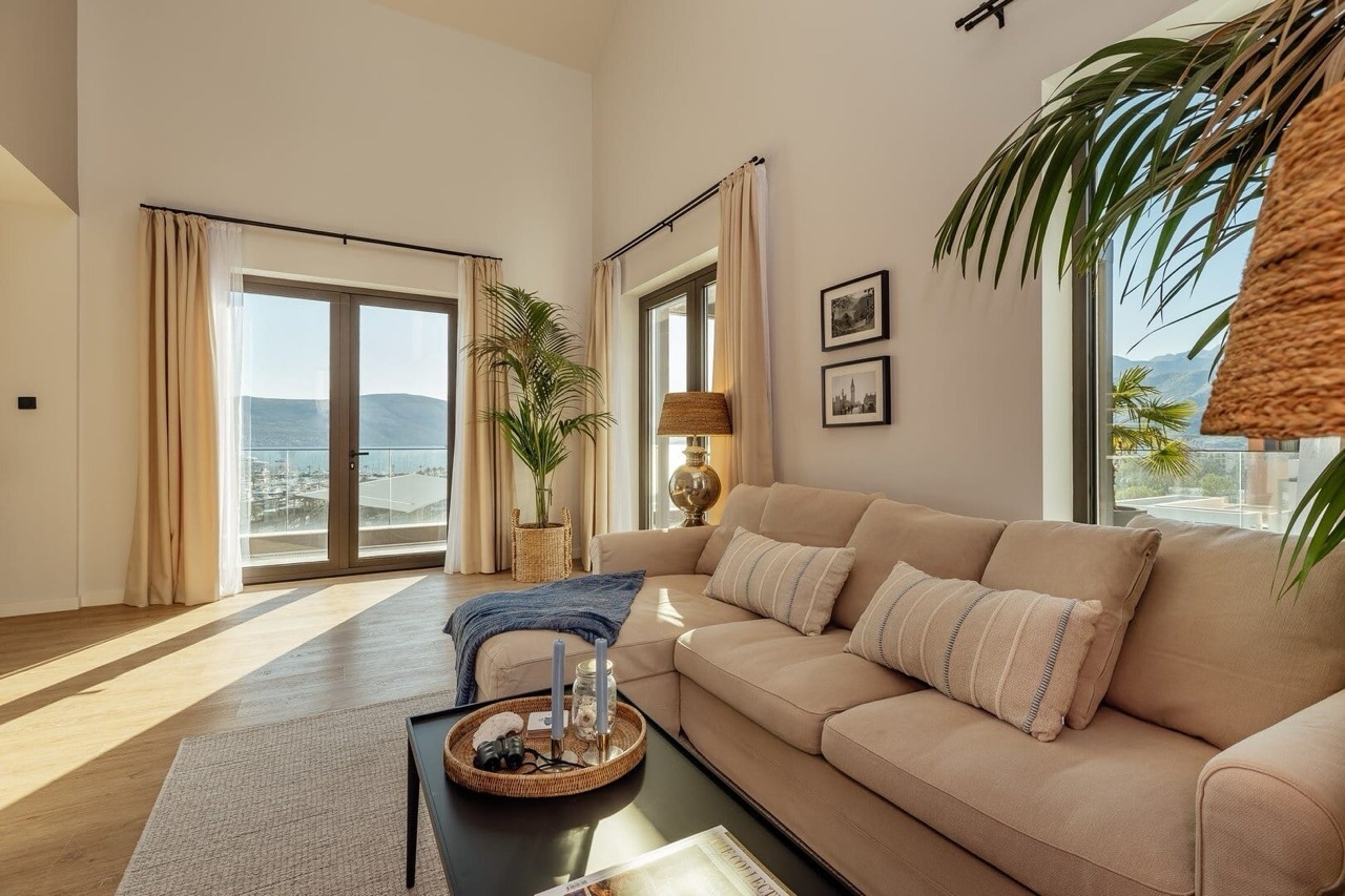 Bright living room in Porto Montenegro, Tivat, Montenegro: beige sofa, panoramic windows with sea and yacht marina views.