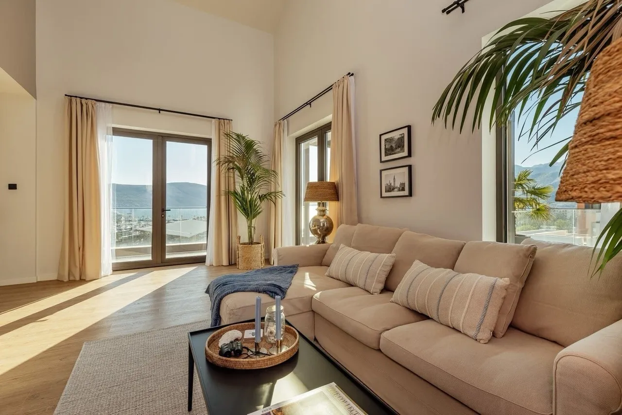 Bright room with a beige sectional sofa, black coffee table, and large windows overlooking the sea.