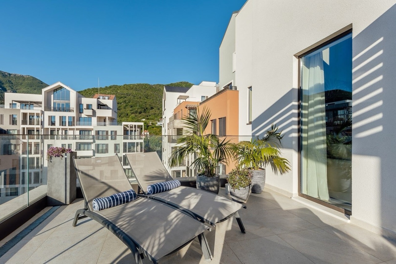 Terrace with sun loungers in an apartment in Porto Montenegro, Tivat, Montenegro: view of modern buildings and mountains.