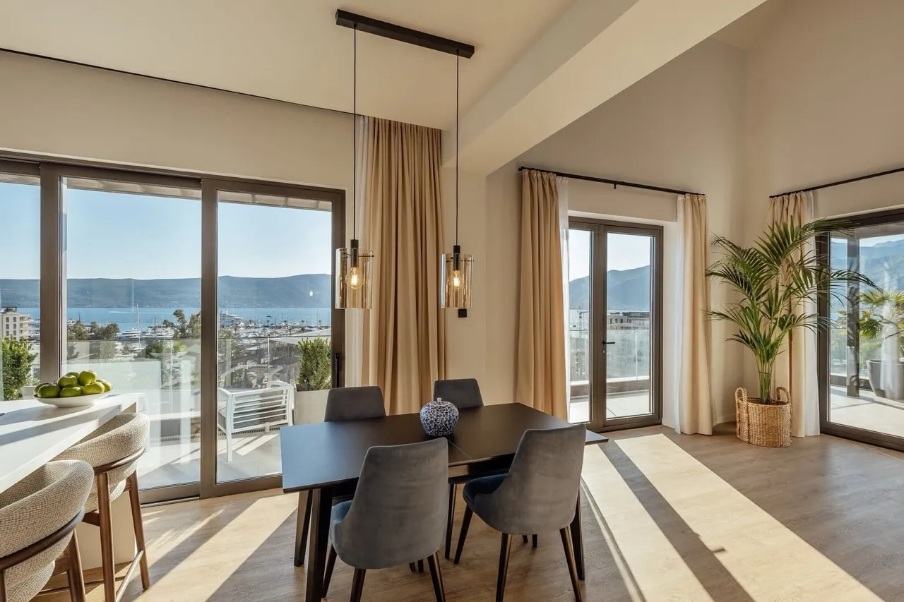 Bright room with a dining table, bar counter, and panoramic windows overlooking the sea and marina.