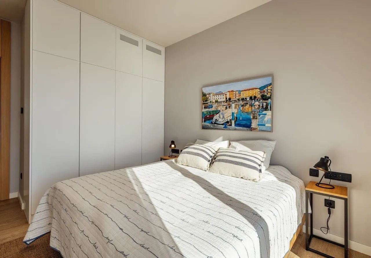 Modern bedroom featuring a double bed, white built-in wardrobes, and a harbor painting above the headboard.