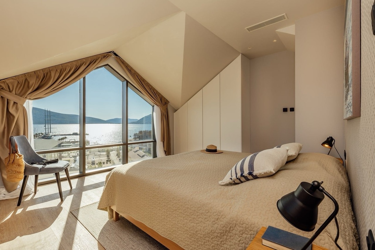 Bedroom in an apartment in Porto Montenegro, Tivat, Montenegro, with panoramic views of the sea, yachts, and mountains through a large window.