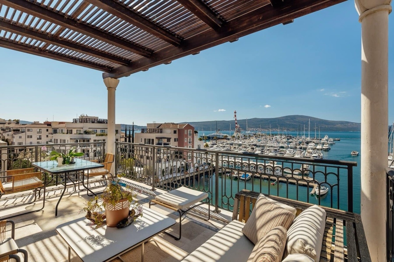 Terrace with furniture and a view of Porto Montenegro yacht marina, Tivat, Montenegro. Sunny balcony with an awning.