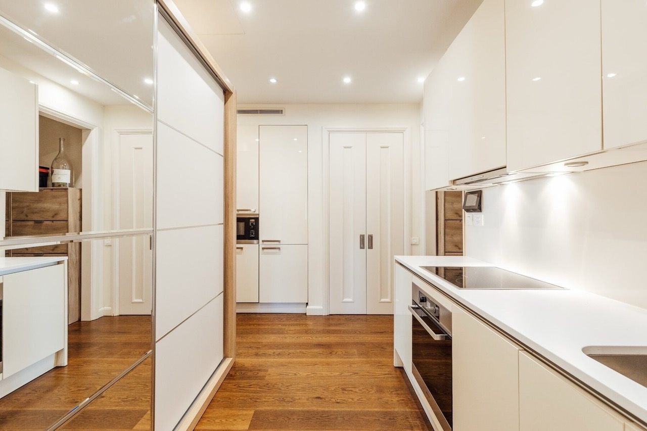Modern kitchen in an apartment in Porto Montenegro, Tivat, Montenegro: white glossy cabinets and wooden floor.