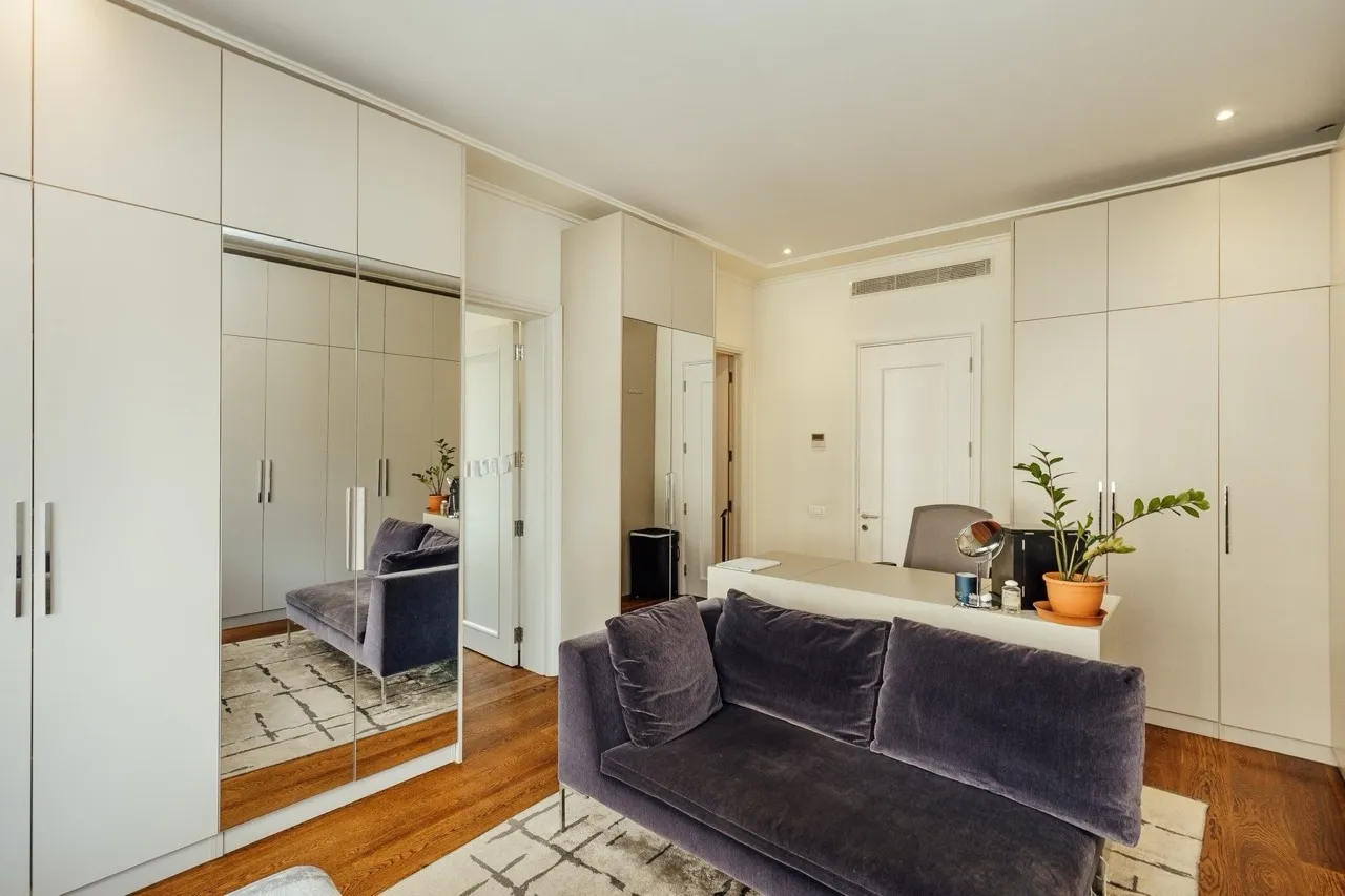 Modern bedroom with white wardrobe cabinets, a purple sofa, and a desk on wooden flooring.