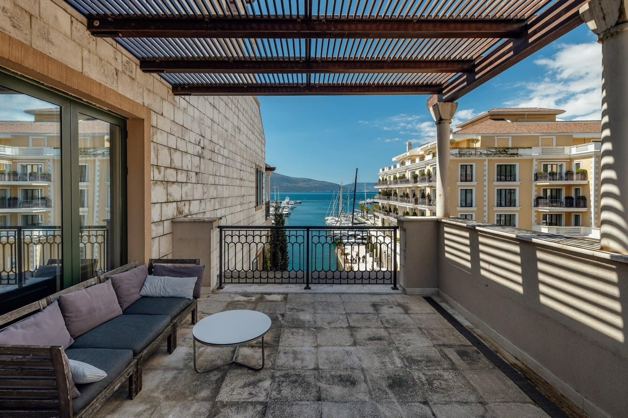 Terrace with furniture and views of the marina and yachts in Porto Montenegro, Tivat, Montenegro. Open loggia with a canopy.