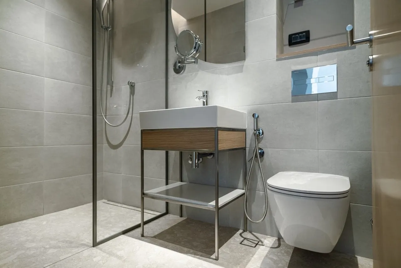 Modern bathroom featuring a wall-mounted toilet, vessel sink on a metal stand, and a glass-enclosed shower area.