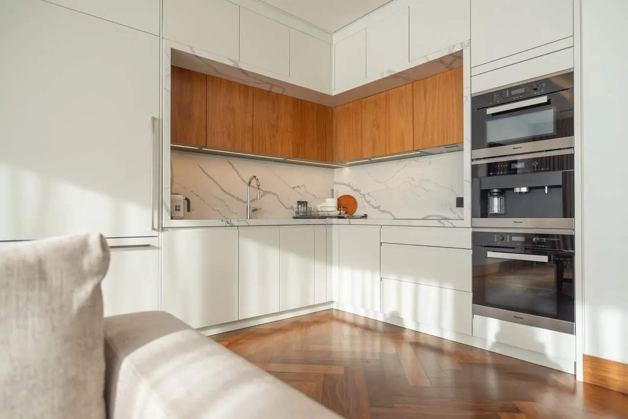 Modern kitchen featuring white and wood cabinets, marble countertops, built-in Miele appliances, and herringbone parquet flooring.