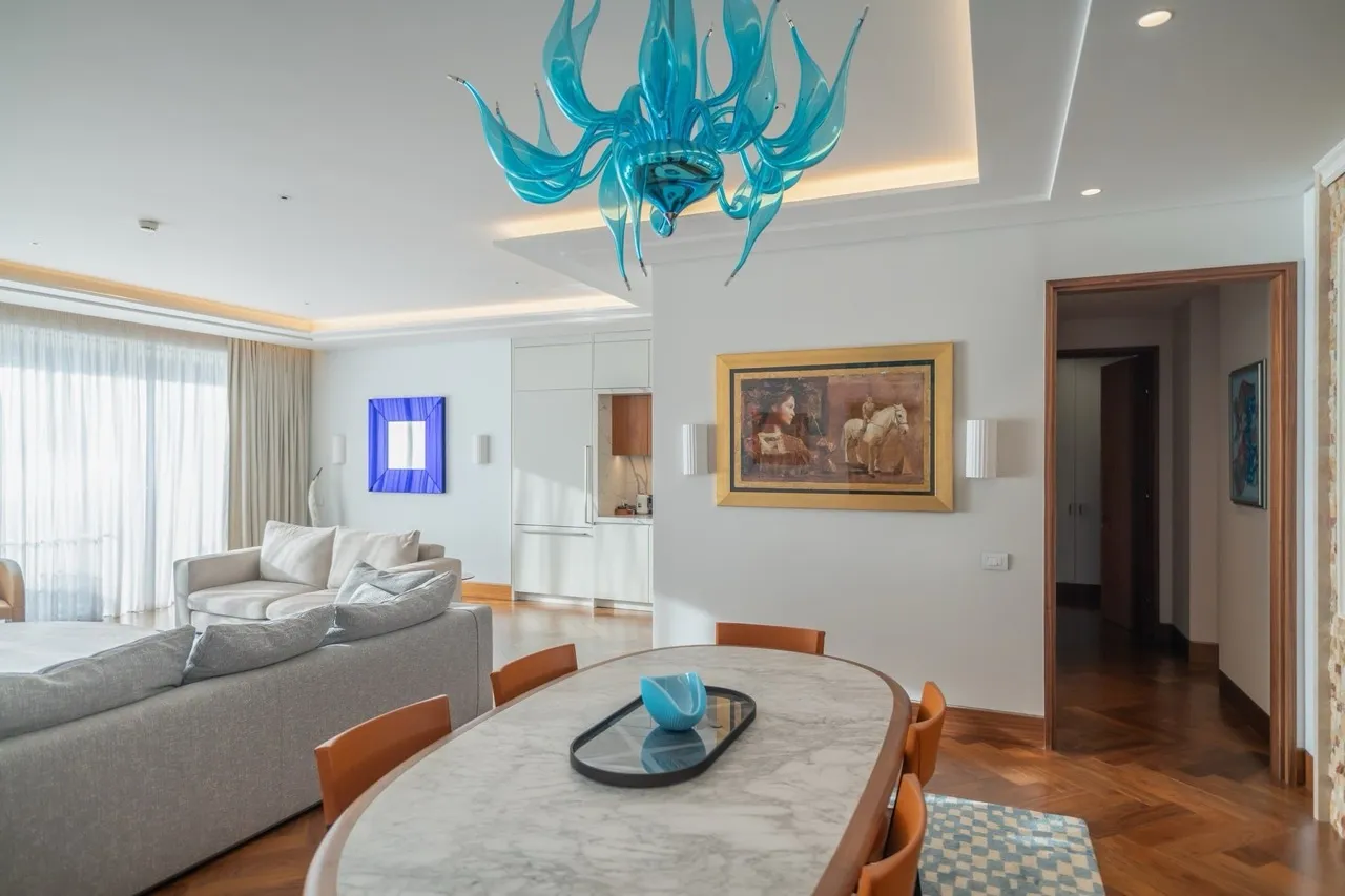 Living room with grey sofa, marble dining table, and distinctive blue glass chandelier overhead.