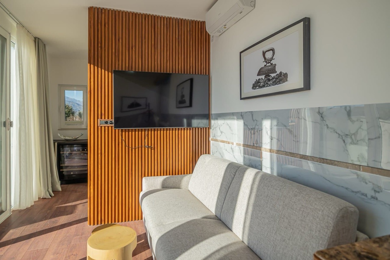 Living room in an apartment in Porto Montenegro, Tivat, Montenegro: gray sofa, TV on a wooden panel, and mountain view.