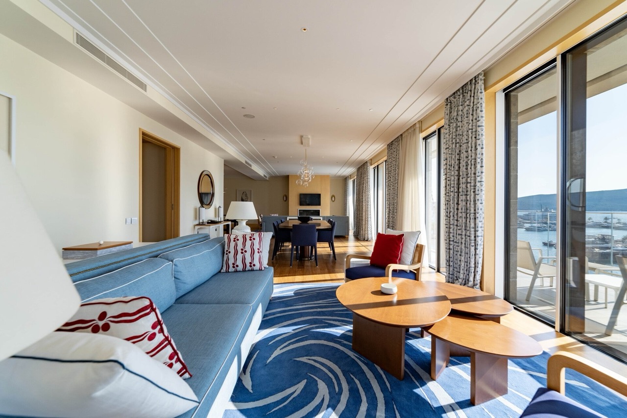 Spacious living room with marina views in a luxury apartment, Tivat, Montenegro: blue sofa, wooden tables, and terrace.