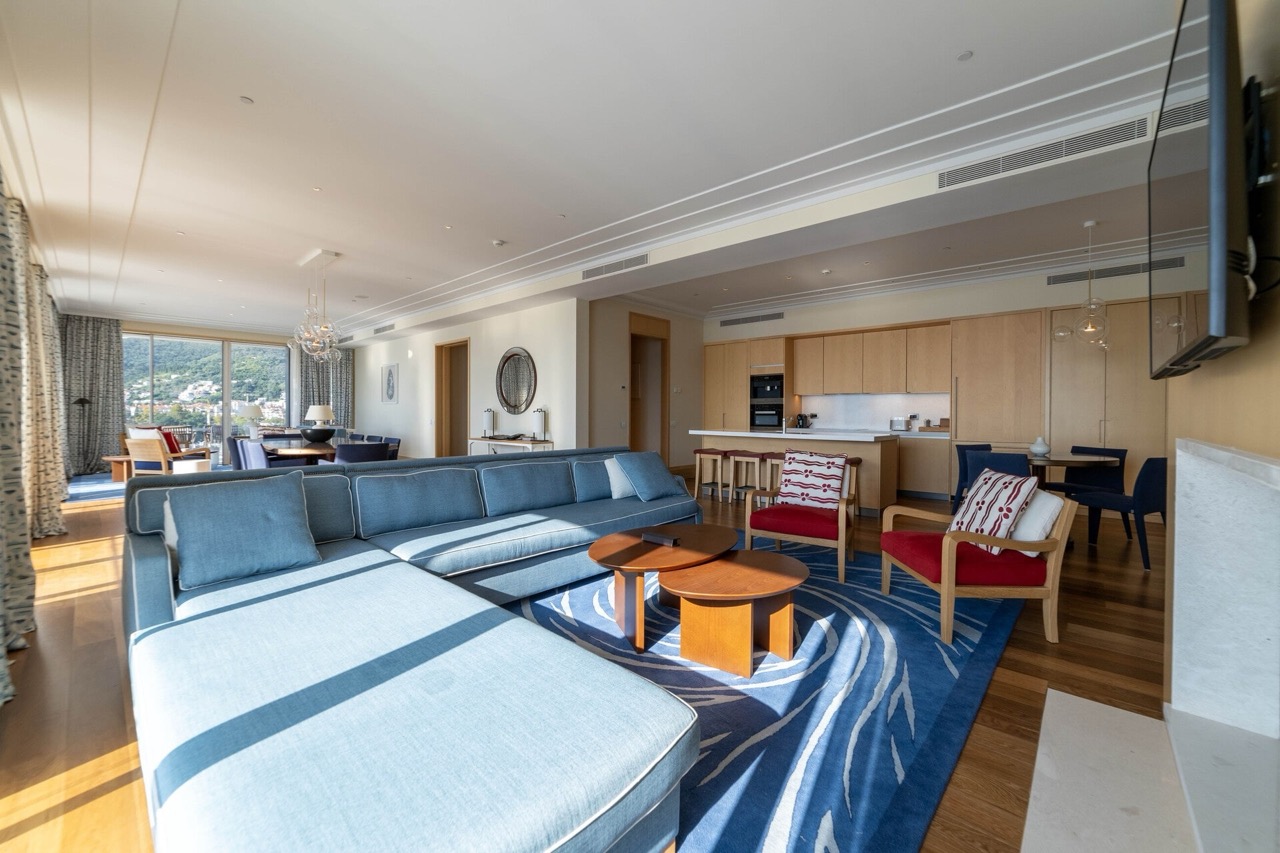 Spacious living room with kitchen in an apartment in Tivat, Montenegro: blue sofa, wooden furniture, and mountain view.