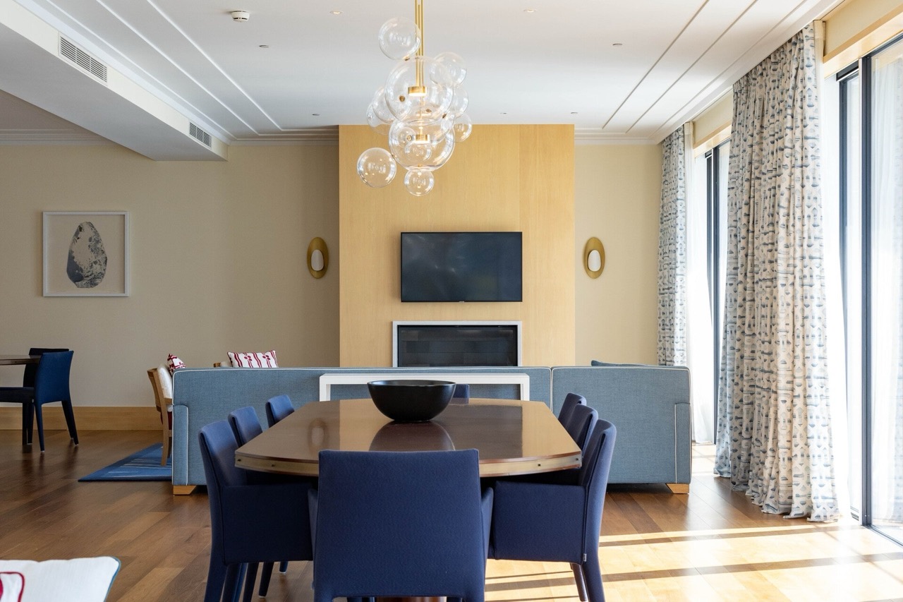 Modern living room with dining area in an apartment in Tivat, Montenegro: blue armchairs, fireplace, and a designer chandelier.