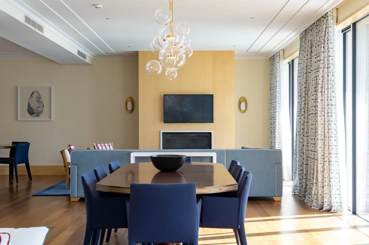 Living room featuring a wooden dining table, blue chairs, sofa, and TV above a fireplace.