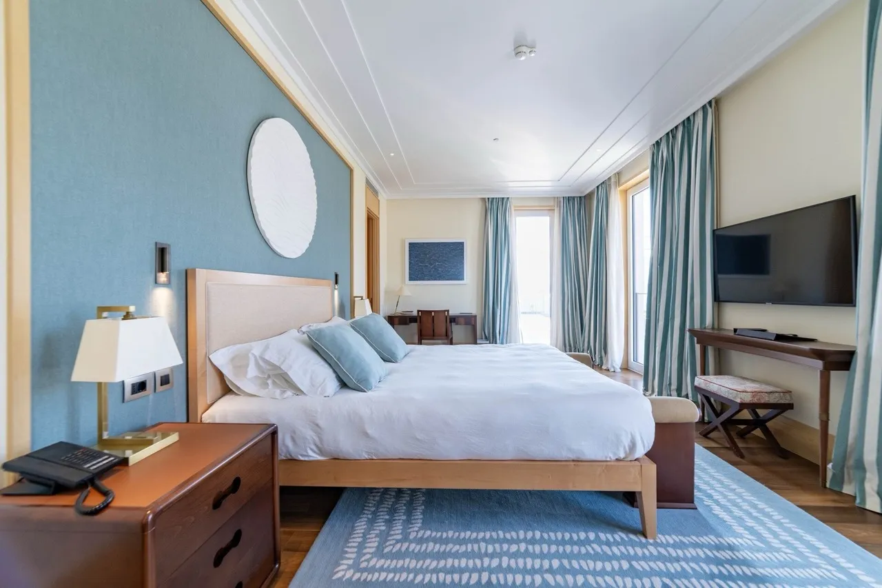 Bedroom featuring a large bed, blue accent wall, nightstand with phone, and TV on a wooden console.