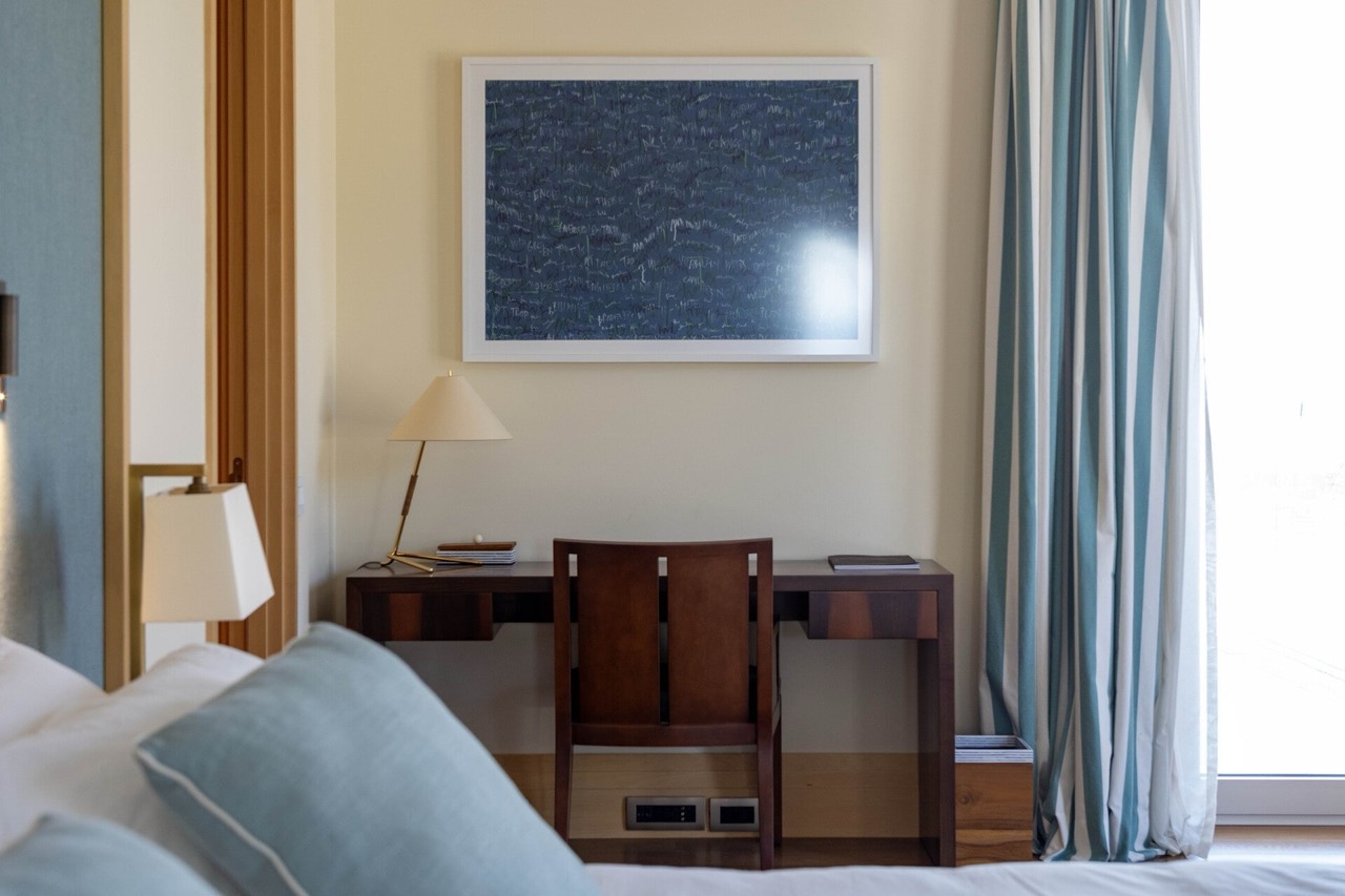 A dark wood desk in the bedroom of a modern apartment in Tivat, Montenegro, with a painting and striped curtains.