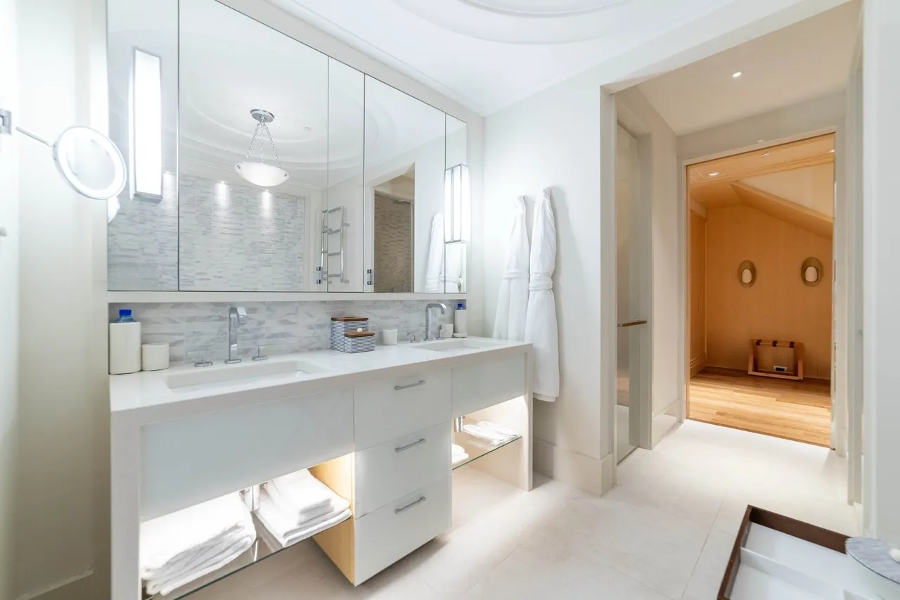 Modern bathroom featuring a double vanity, large mirror, white robes, and tiled flooring.
