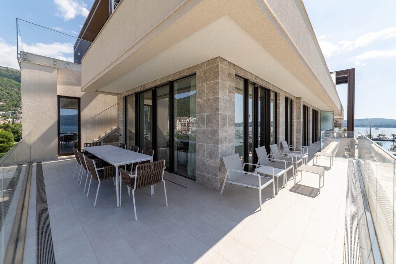 Spacious apartment terrace in Tivat, Montenegro, with a dining area, modern furniture, and panoramic sea views.
