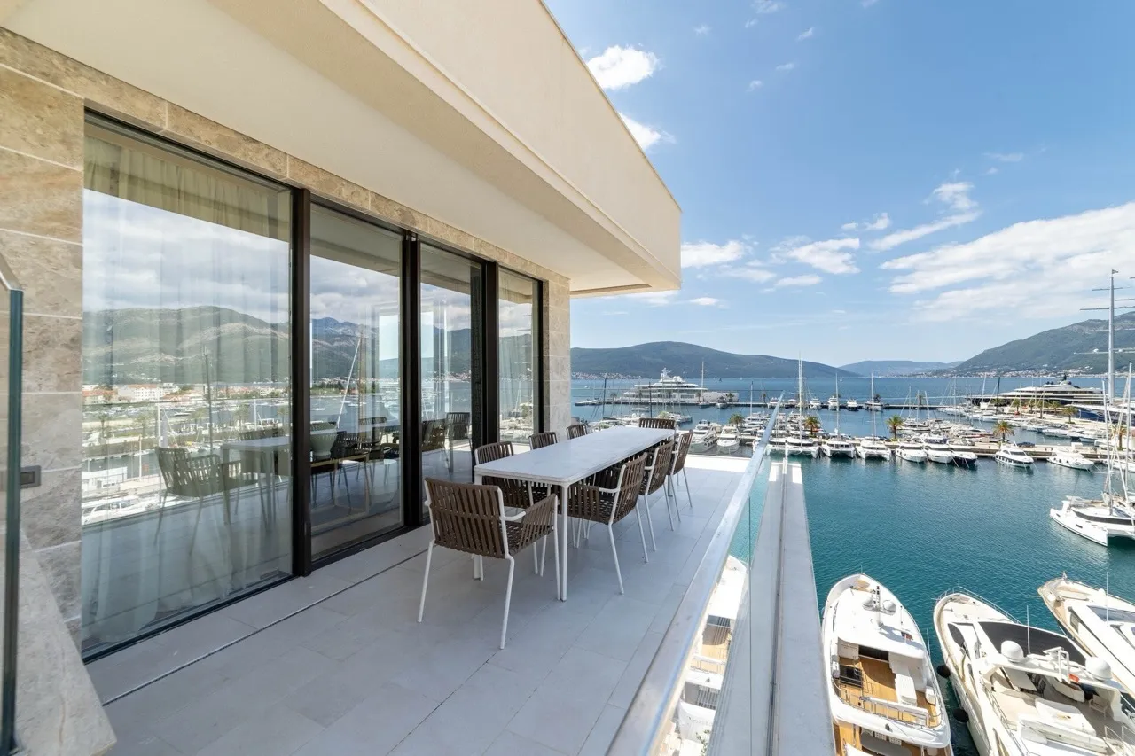 Balcony with dining set overlooking a marina filled with boats and mountains.