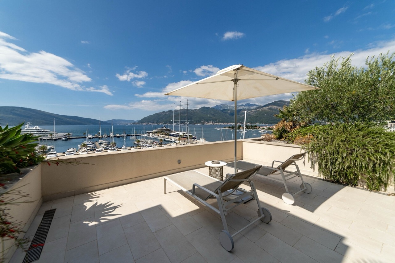 Terrace with sun loungers and an umbrella in an apartment in Tivat, Montenegro, with panoramic views of the marina and mountains.