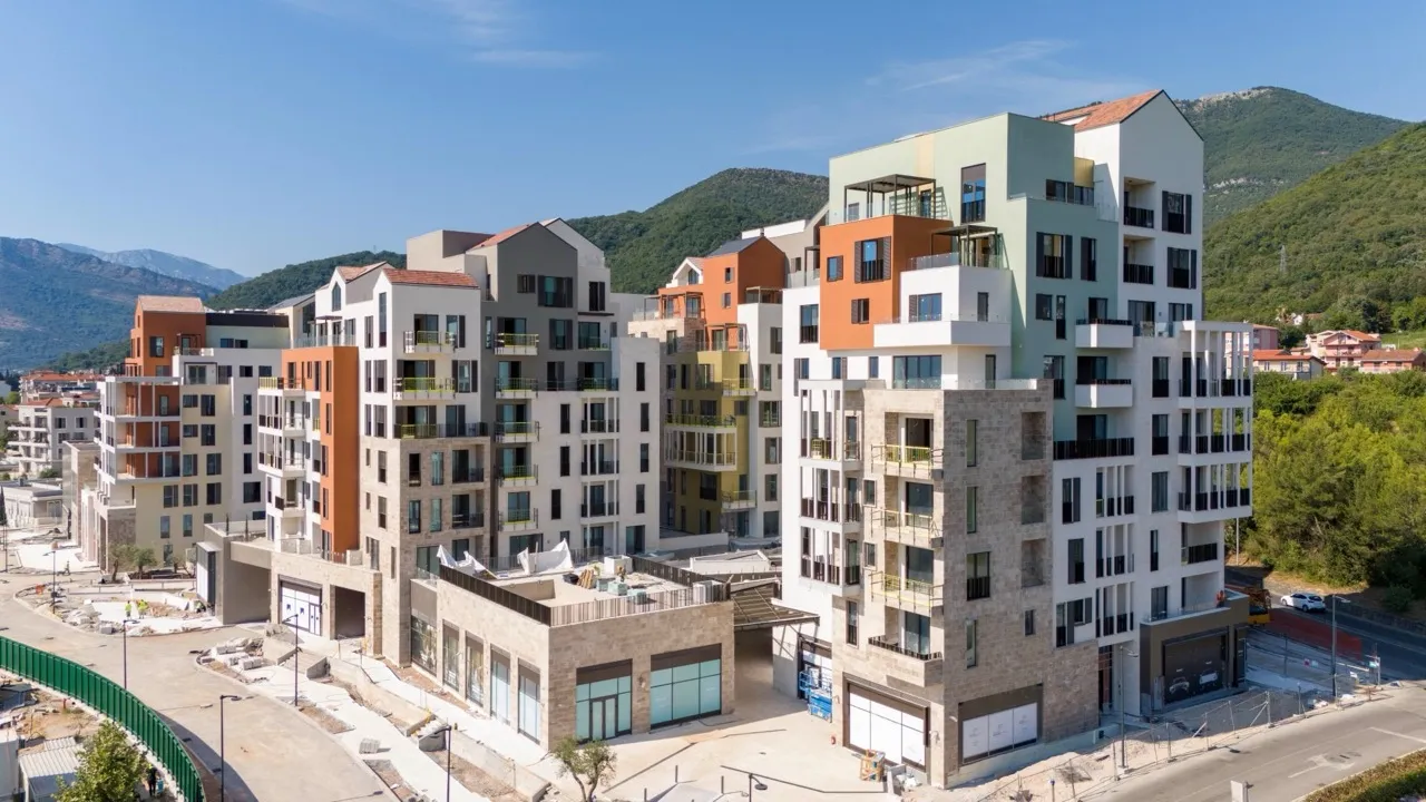 Aerial view of a modern multi-story apartment complex with colorful facades and mountains.