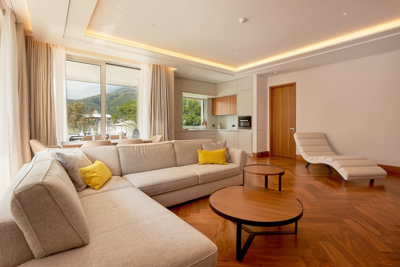 Modern living room with kitchen in Porto Montenegro, Tivat, Montenegro: light furniture, parquet flooring, and mountain views.