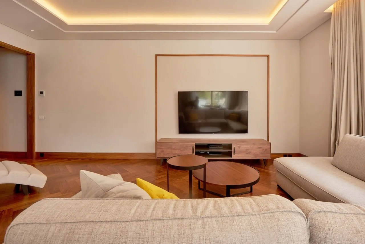 Living room with beige sofa, wooden parquet, round table, and TV on a media console.