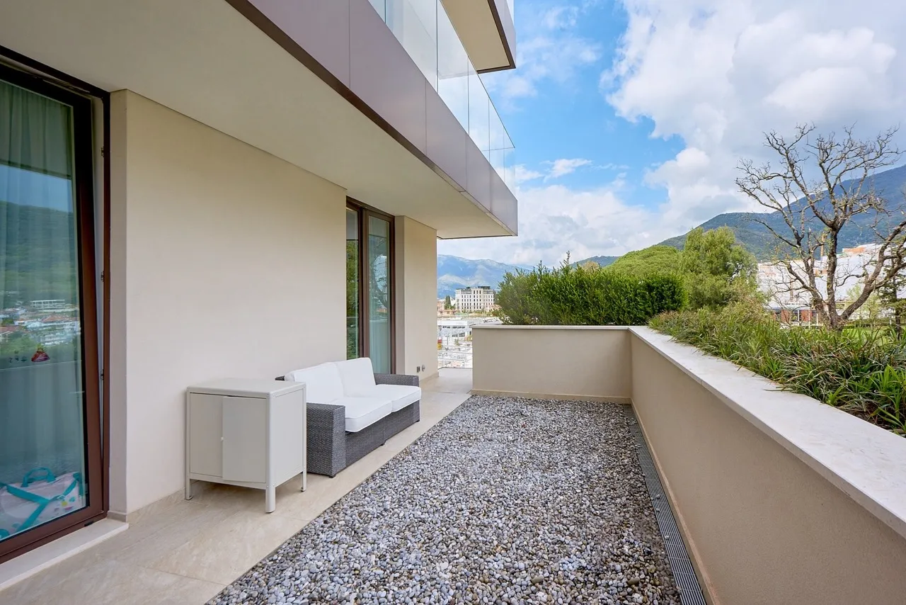 Modern balcony with gravel flooring, wicker sofa, and white cabinet overlooking mountains.