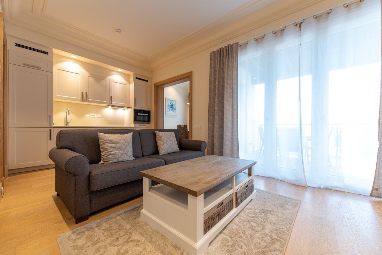 Living room with kitchen in an apartment in Porto Montenegro, Tivat, Montenegro: gray sofa, wooden table, and panoramic windows.
