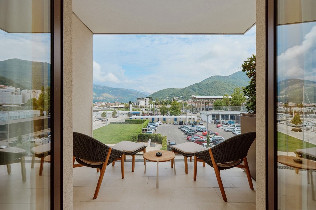 View from the apartment balcony in Porto Montenegro, Tivat, Montenegro: wicker furniture and a panoramic view of the mountains and marina.