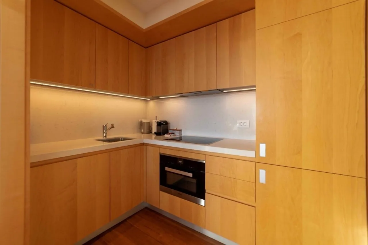 Modern kitchen with light wood cabinets, white countertop, built-in oven, sink, and induction cooktop.