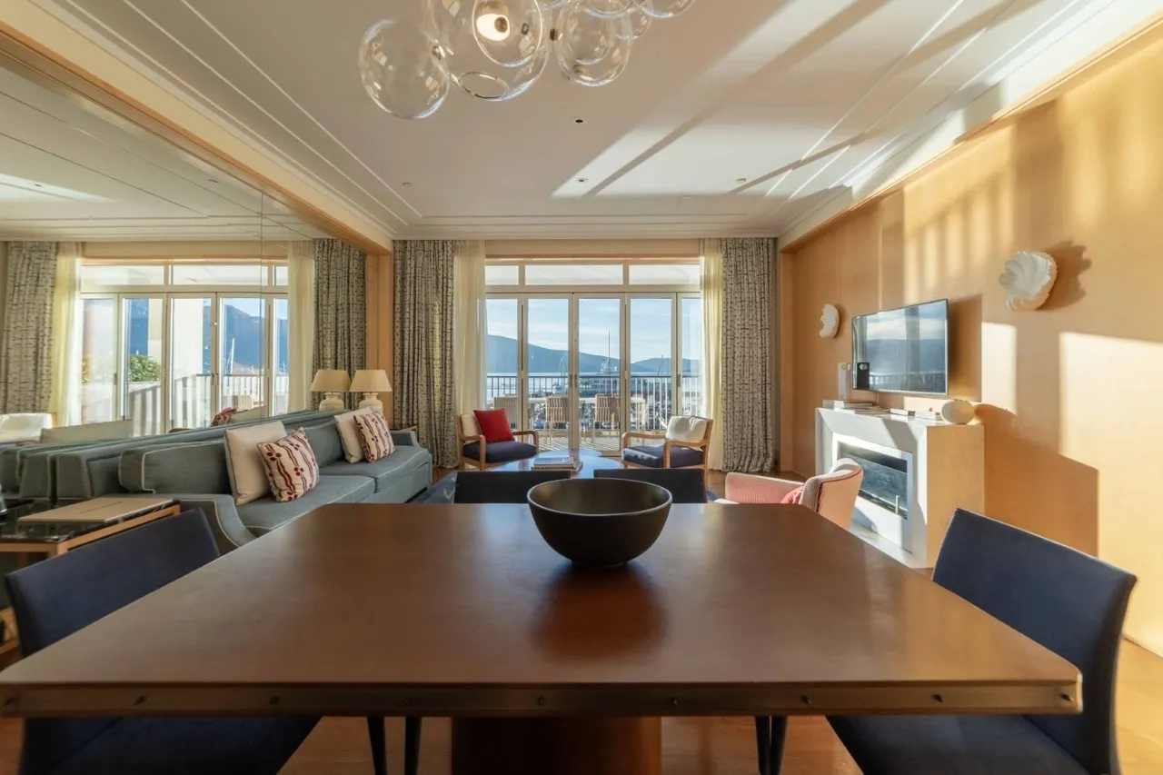 Living room with dining table, sofa, TV, and fireplace. Large windows show a balcony view.