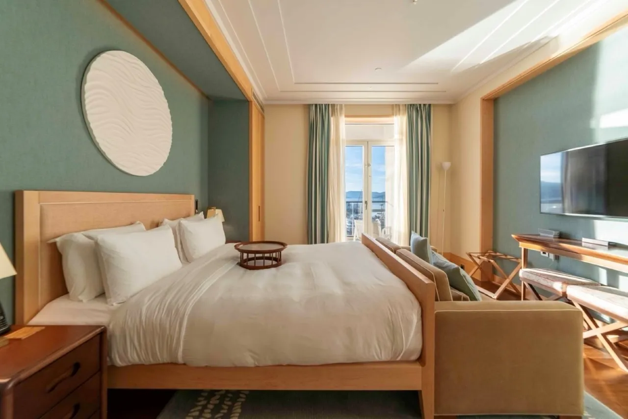 Modern bedroom featuring a large wooden bed with white linens, a wall-mounted TV, and teal accent walls.