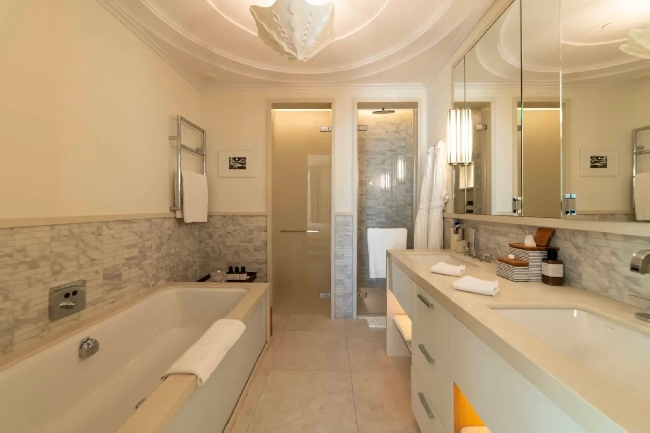 Bright bathroom featuring a bathtub, double vanity, glass shower, and marble tile accents.