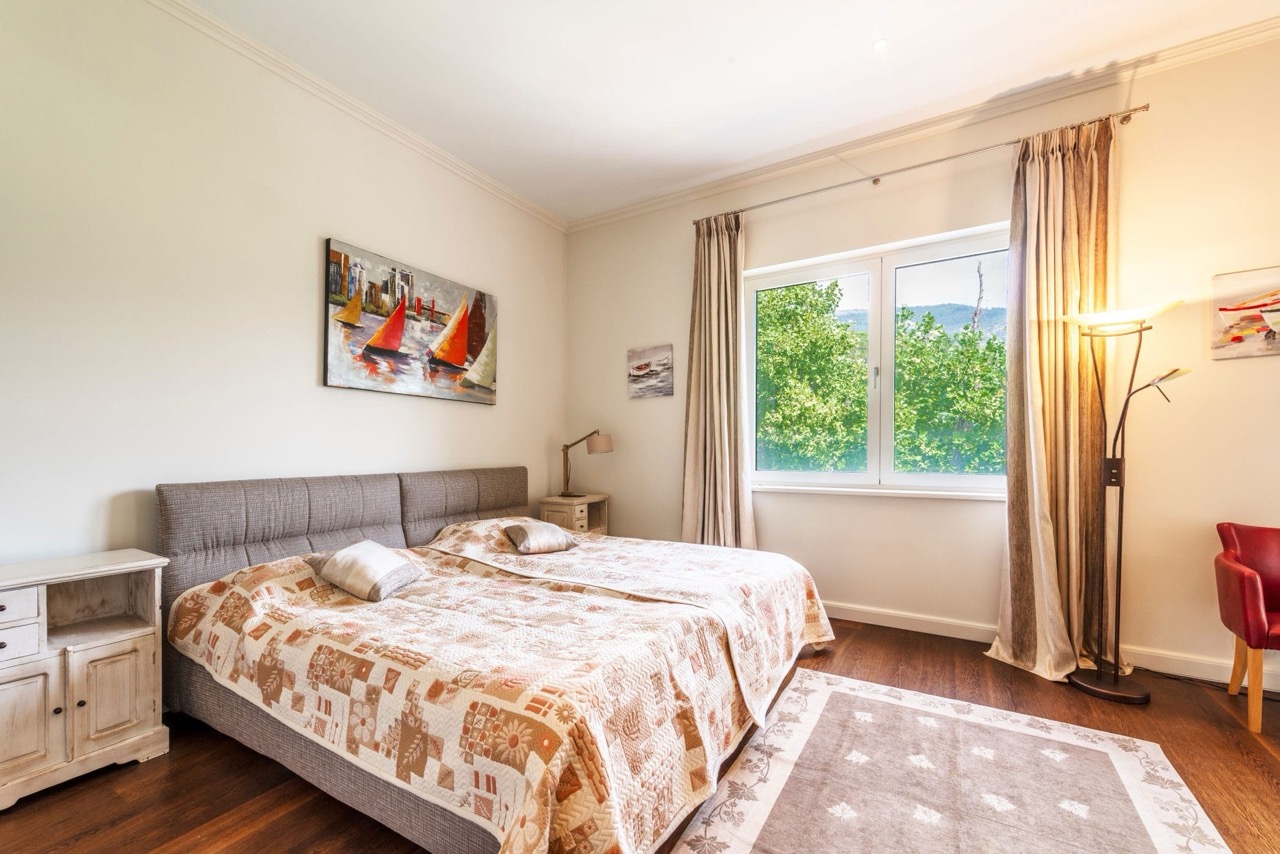 Cozy bedroom in an apartment in Porto Montenegro, Tivat, Montenegro: double bed, parquet flooring, and a view of greenery from the window.