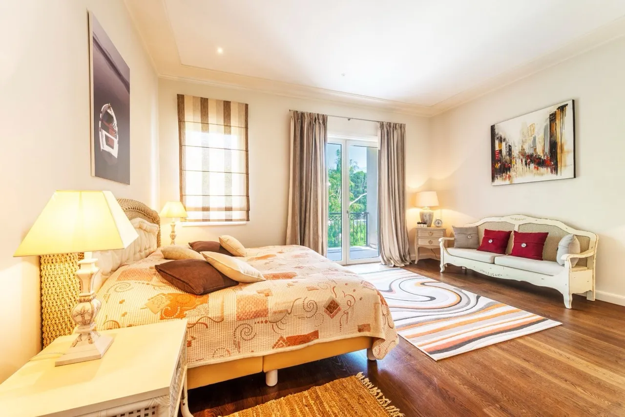 Bedroom featuring a large bed with patterned bedding, a white sofa, and glass doors leading to a balcony.