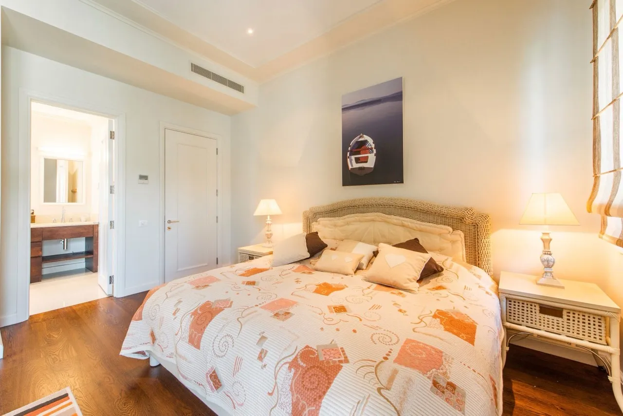 Bright bedroom featuring a large bed with a woven frame, patterned coverlet, and an attached bathroom visible through the door.