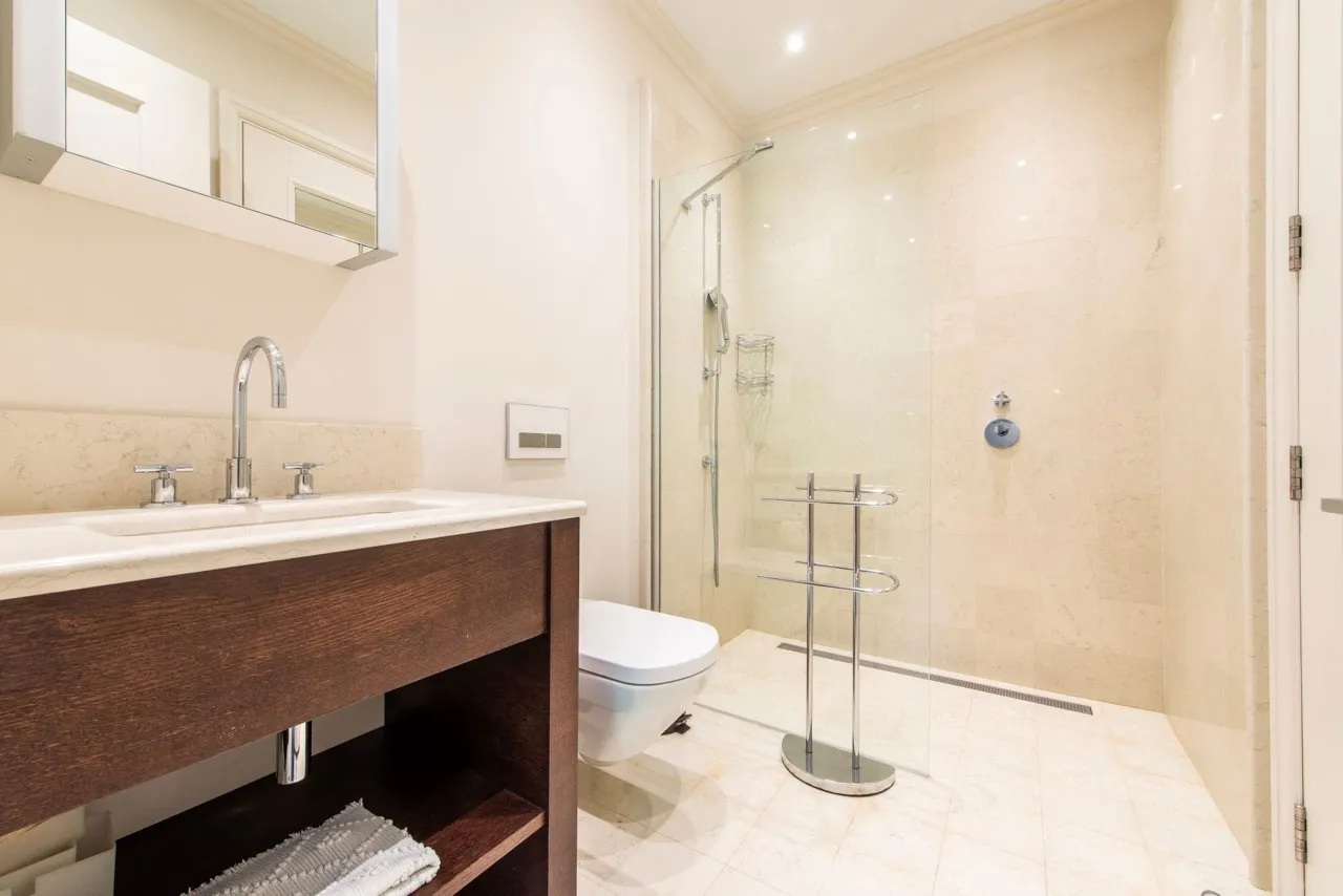 Modern bathroom featuring a glass shower enclosure, wall-mounted toilet, and wooden vanity with sink.
