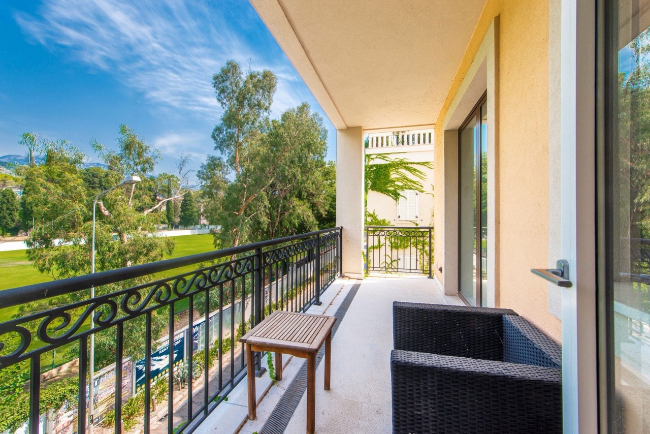 Balcony with wicker furniture in an apartment in Porto Montenegro, Tivat, Montenegro, overlooking the green area and mountains.