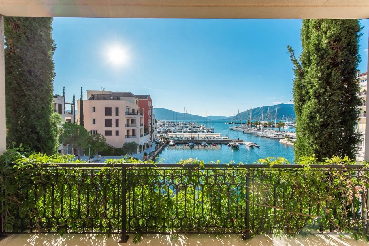 View from a balcony with green railing overlooking a marina filled with boats and distant mountains.