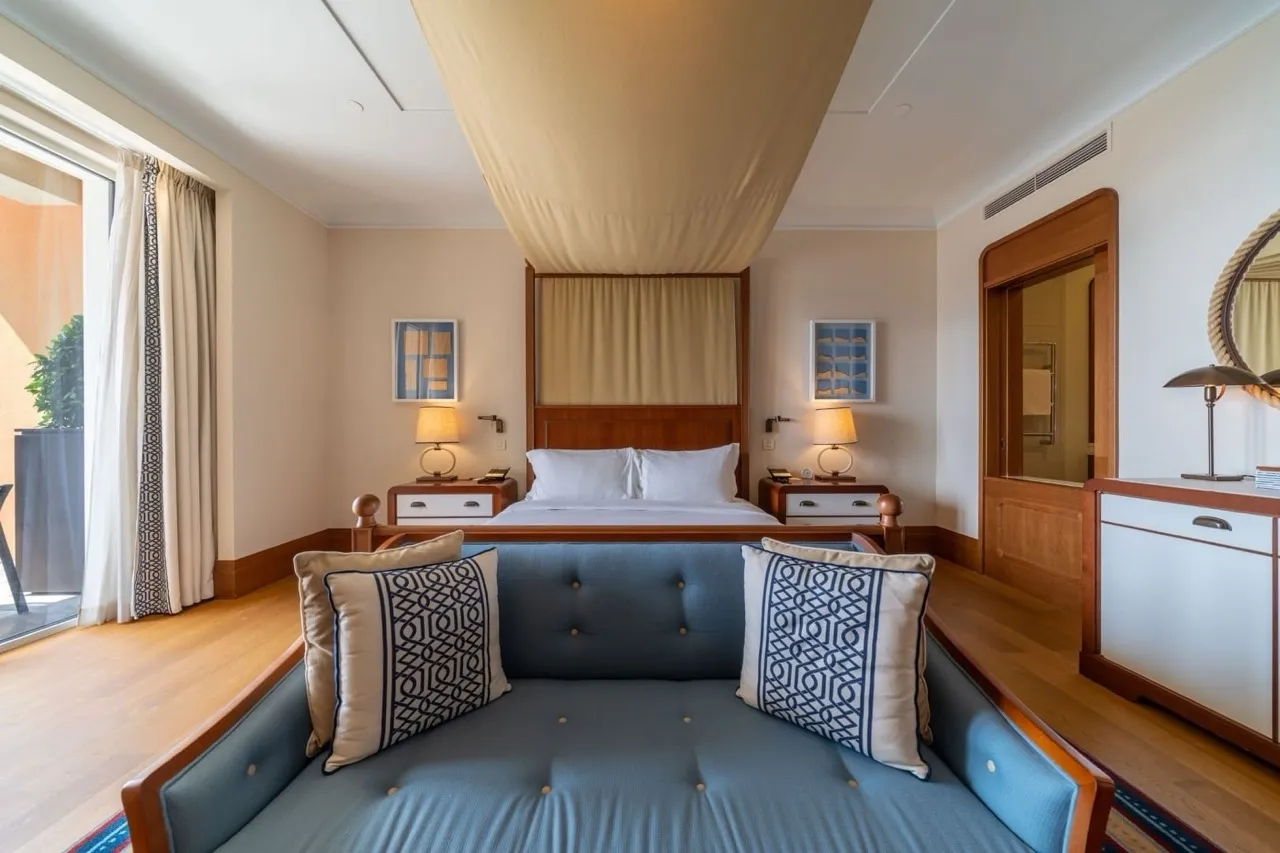 Bedroom featuring a canopy bed, blue sofa in foreground, and wooden nightstands with lamps.