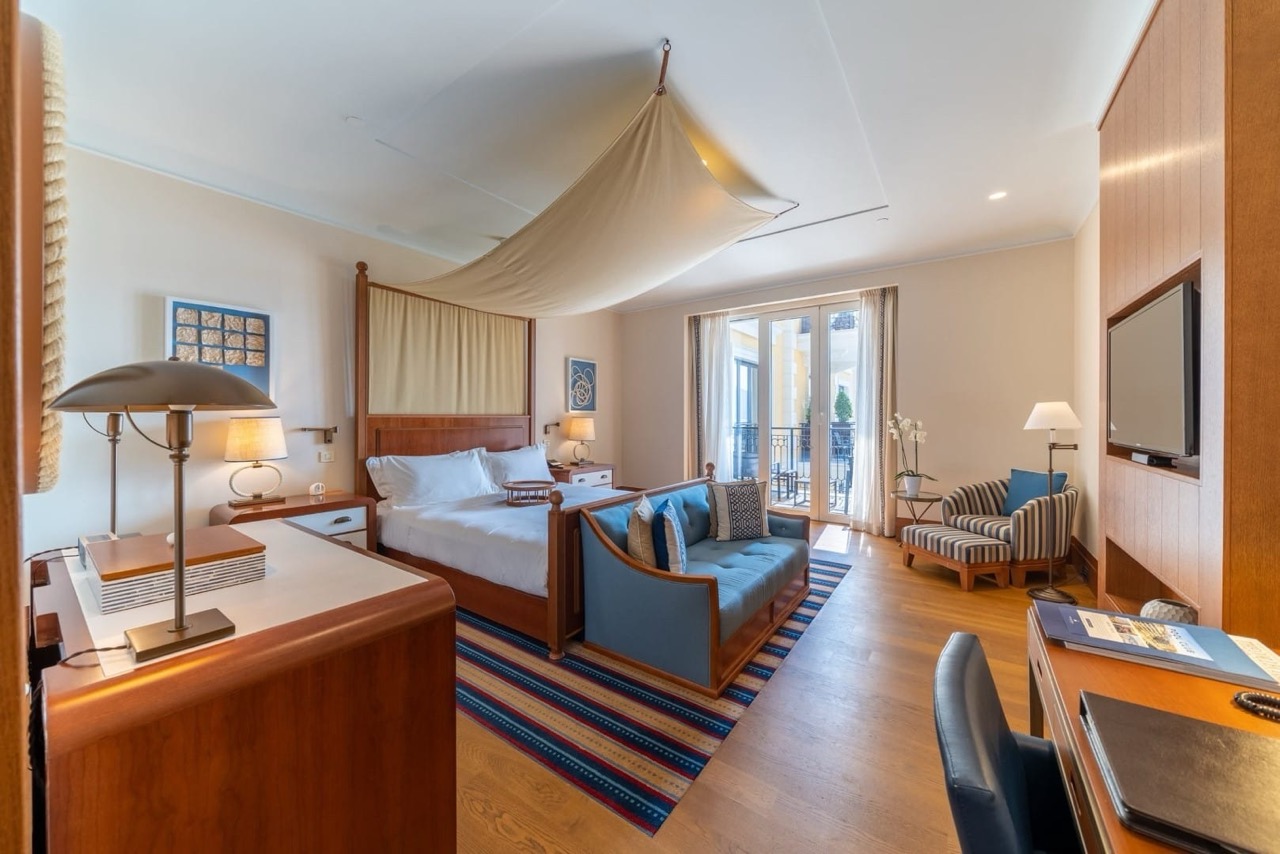 Bedroom interior in Porto Montenegro apartments, Tivat, Montenegro: canopy bed, blue sofa, and view of the terrace.