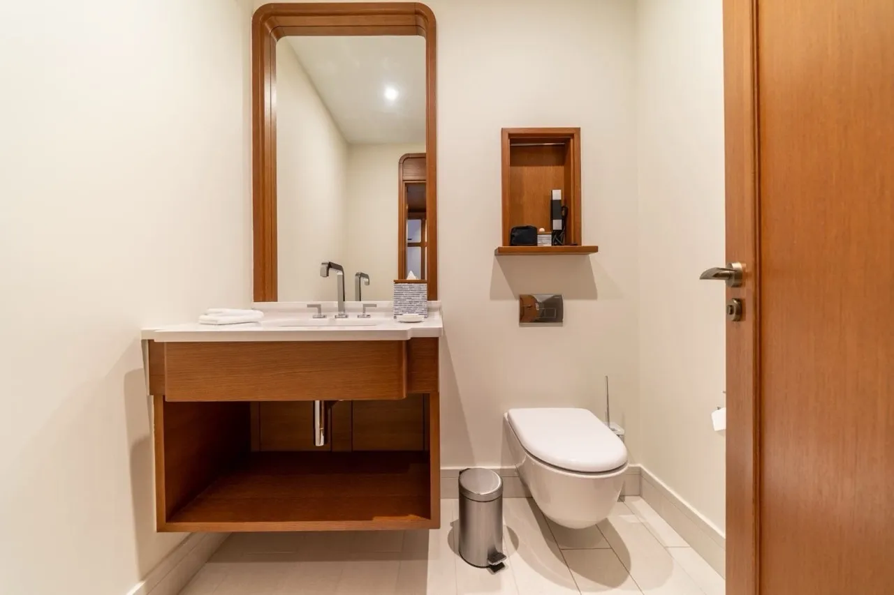 Modern bathroom featuring a wall-mounted toilet, wooden vanity with sink, and a large framed mirror.