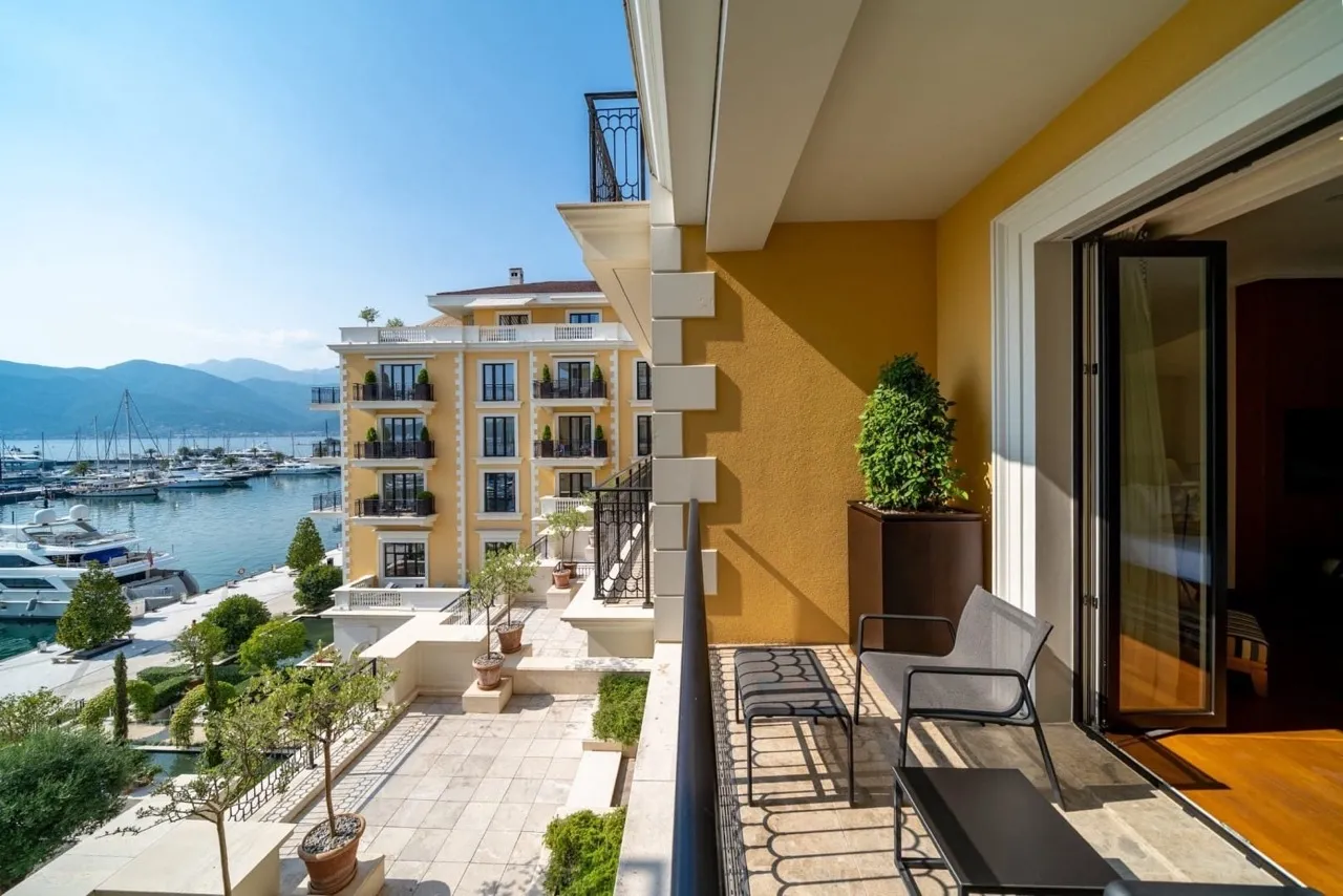 Balcony with a view of the marina and yachts, yellow wall, metal furniture, and open door.