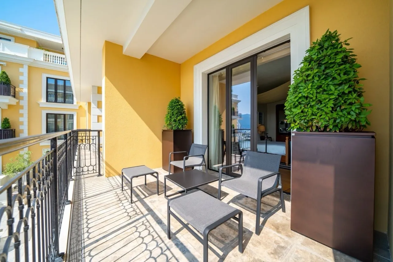 Outdoor balcony featuring grey seating, yellow walls, potted green plants, and a sliding glass door leading inside.