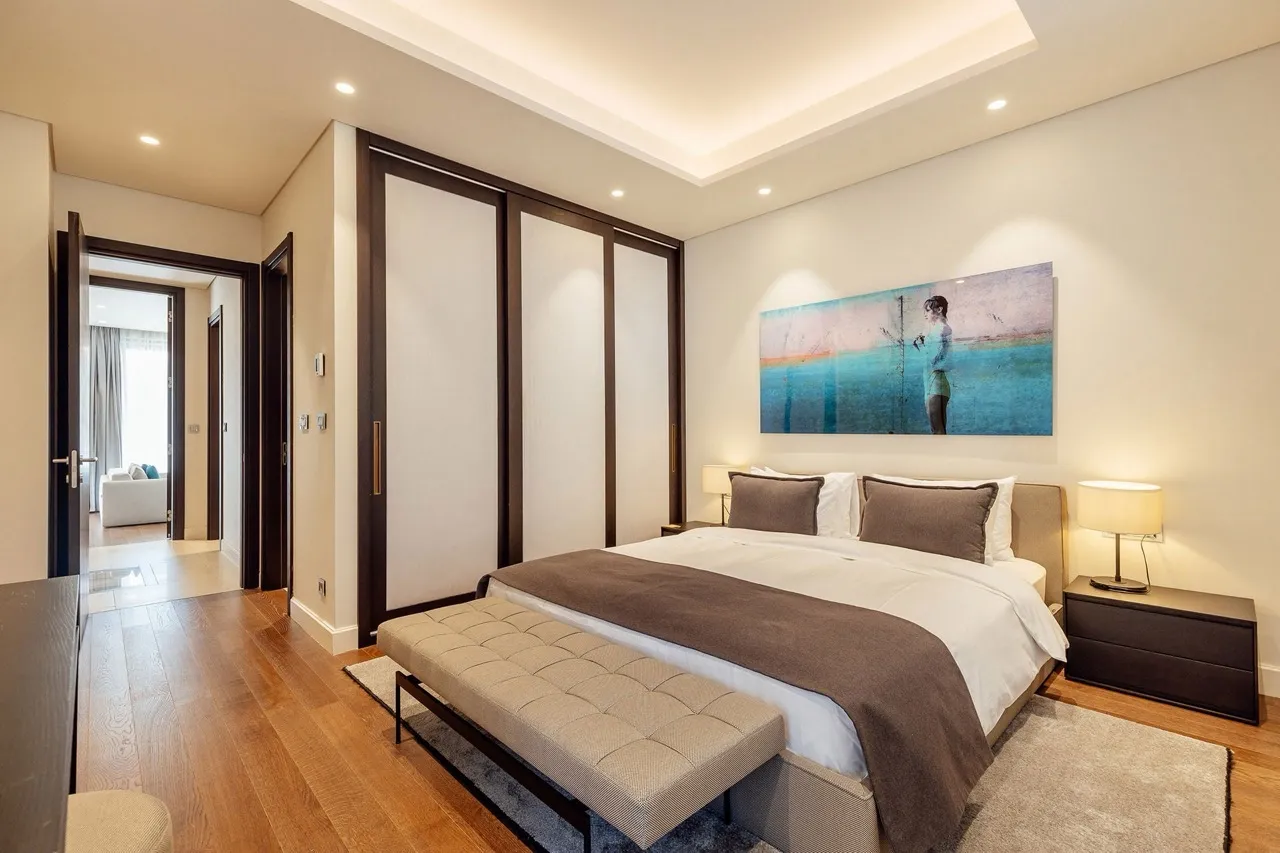 Modern bedroom featuring a double bed, upholstered bench, sliding wardrobes, and wall art above the headboard on wood flooring.