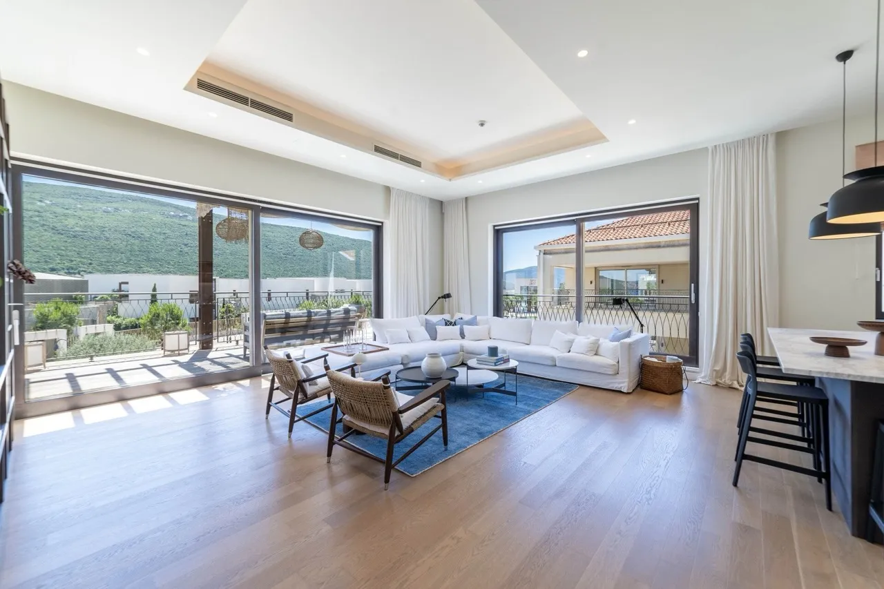 Bright living room with white sofa, blue rug, and large windows overlooking a balcony.