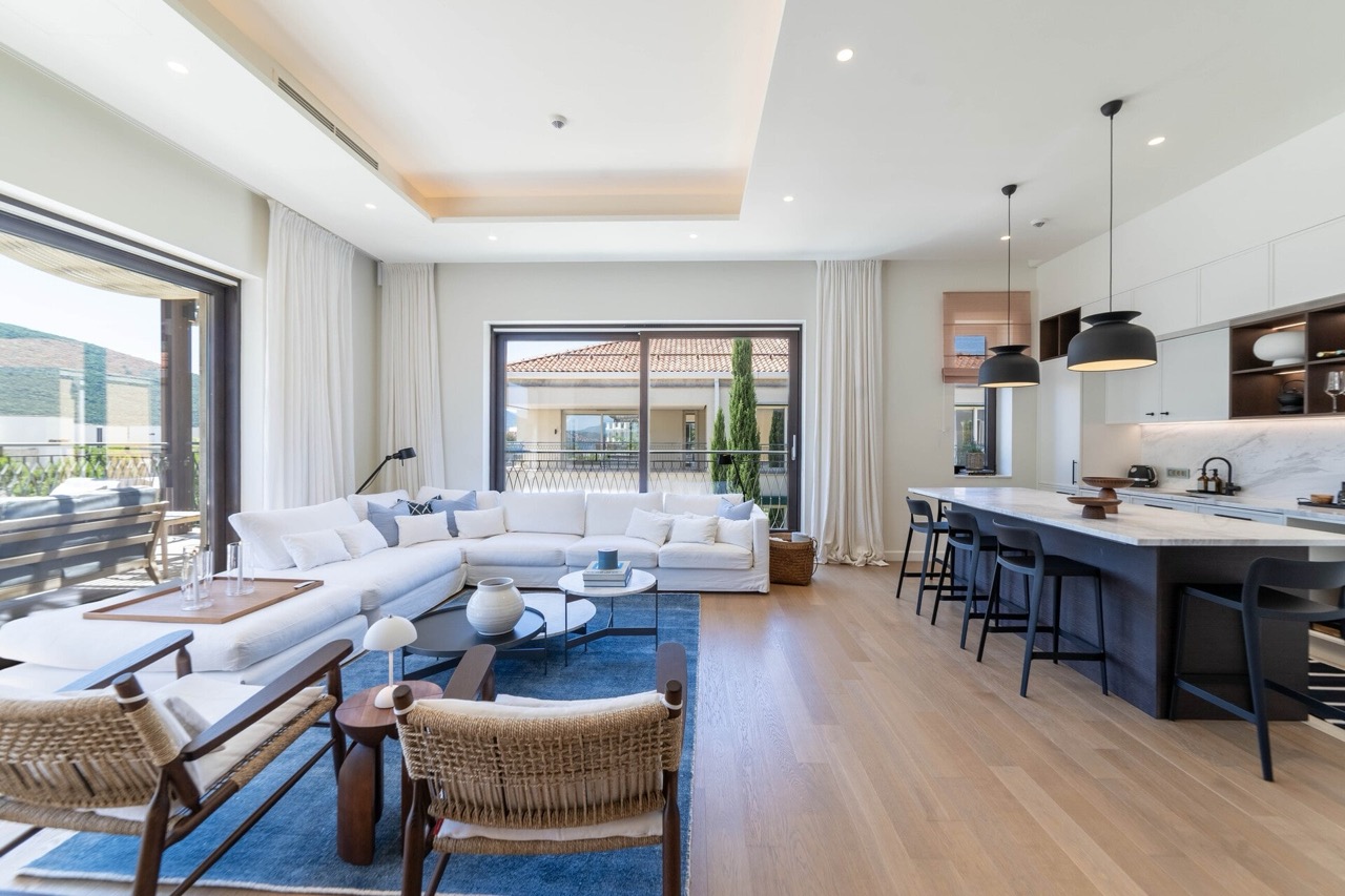 Modern living room with kitchen in an apartment in Portonovi, Kumbor, Montenegro: white sofa, island, and panoramic windows.
